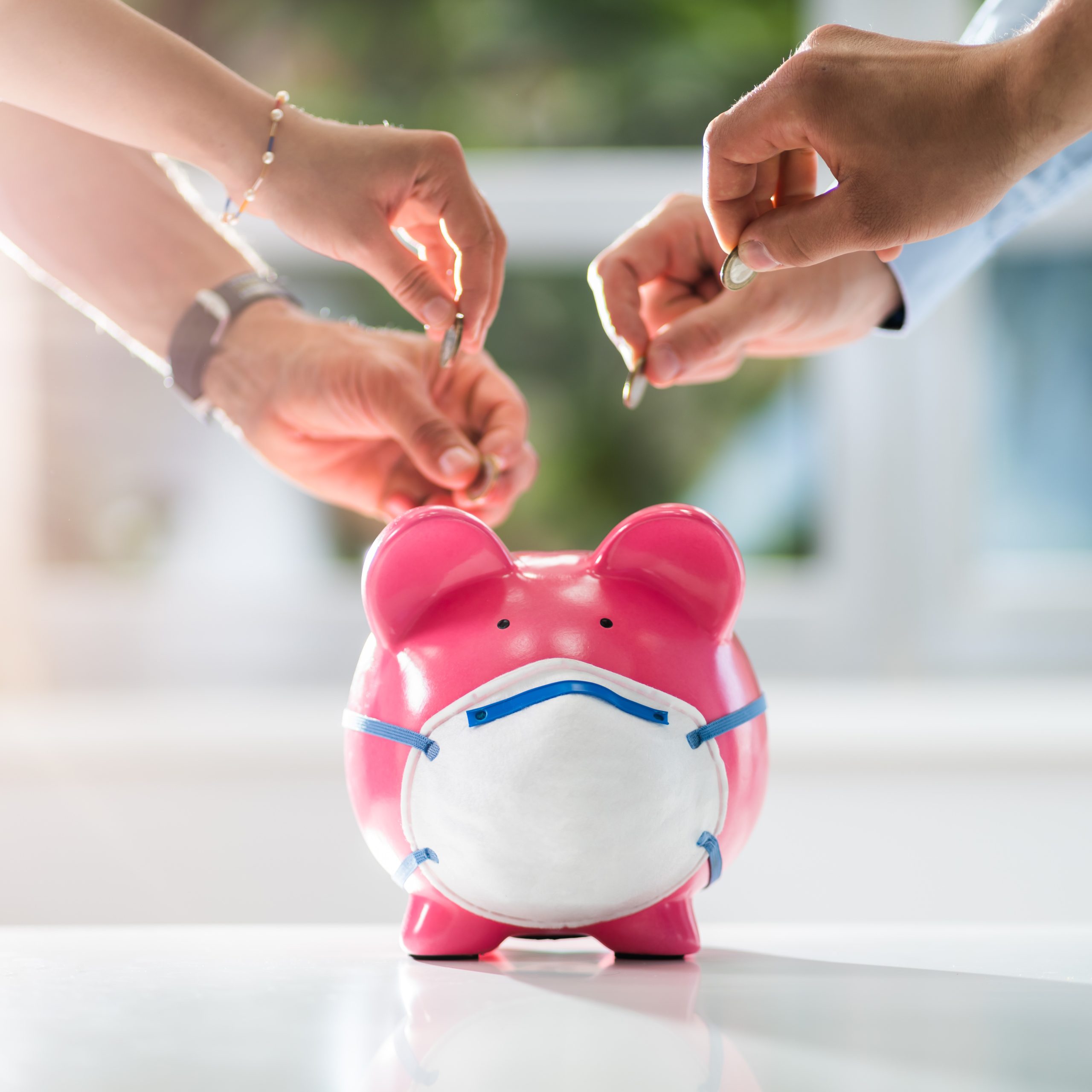 A group of hands putting coins into a piggy bank.